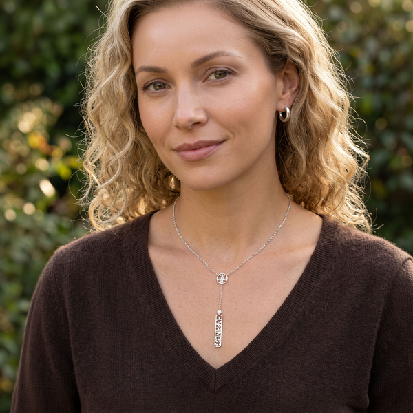 A woman with blonde curly hair wearing a silver lariat-style pendant necklace with a vertical bar with the word 'BELIEVE' amd a Kanji character translating the word Believe above and Bezel set diamond.