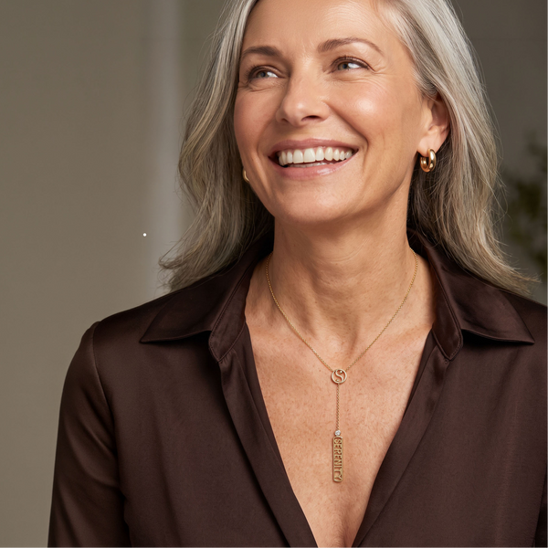 A smiling woman wearing a gold necklace with a vertical bar pendant with a Yin Yang symbol and the word 'Serenity."
