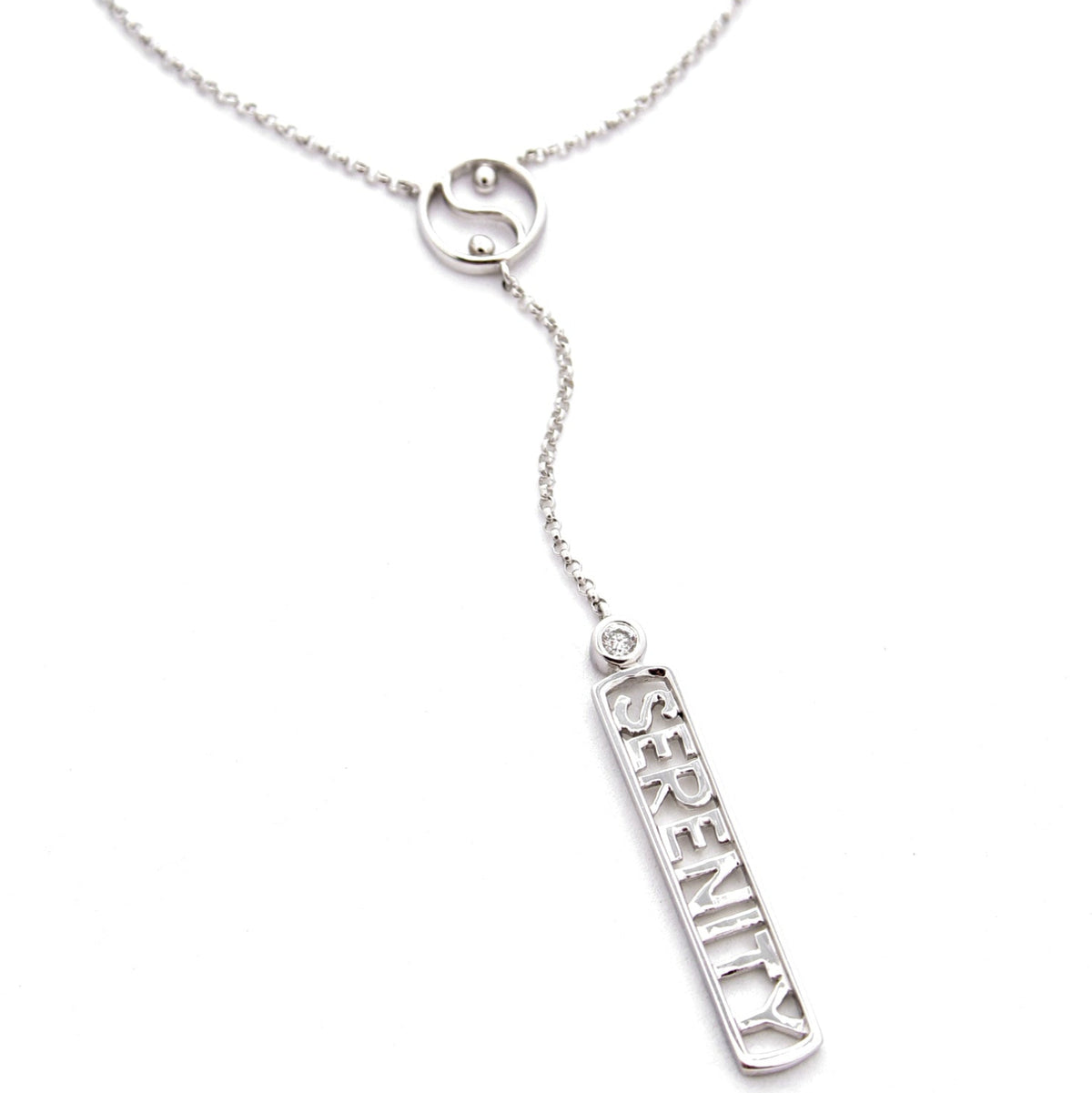 A sterling silver 'Y' necklace featuring a delicate chain with a small circular yin-yang symbol and a dangling rectangular bar with the word 'SERENITY' and a bezel set diamond, shown on a plain white background.